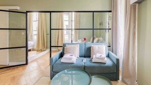 A modern living room with a blue sofa, a glass coffee table, and a sliding glass door leading to a balcony.