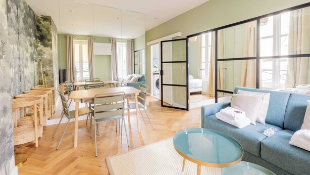 A modern hotel room with a dining area, a sofa, and a glass partition.