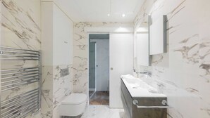 A modern bathroom with a marble backsplash, a toilet, a sink with a mirror, and a shower area.