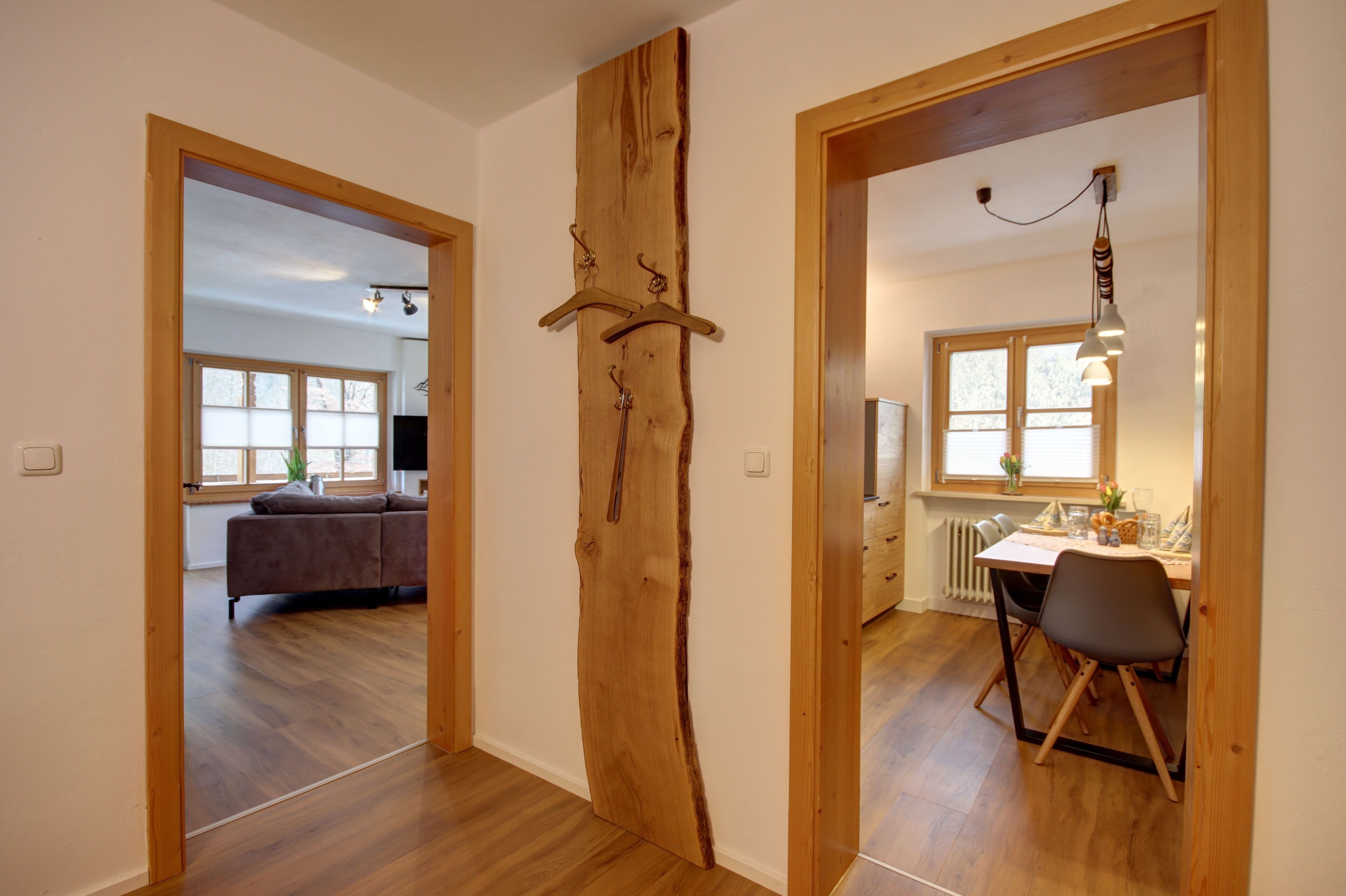 Ein modernes Interieur mit einer Holztür, einem Essbereich mit Tisch und Stühlen sowie einem Wohnzimmer mit Sofa und Fernseher.