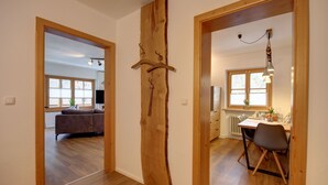 Ein modernes Interieur mit einer Holztür, einem Essbereich mit Tisch und Stühlen sowie einem Wohnzimmer mit Sofa und Fernseher.