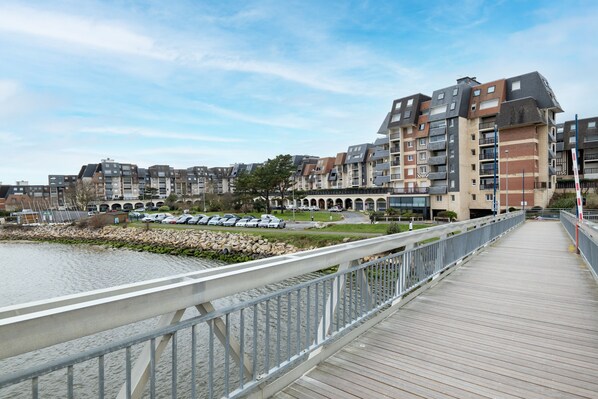 A modern apartment building with multiple balconies, a wooden boardwalk, and a parking area.