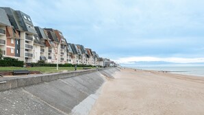 Un hotel frente a la playa con varios edificios, una playa arenosa y un paseo marítimo.