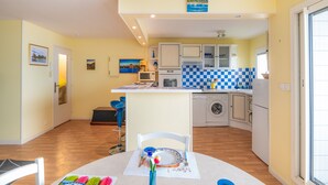 Una cocina compacta con una isla central, un comedor con una mesa lista para dos personas y una lavadora en la esquina.