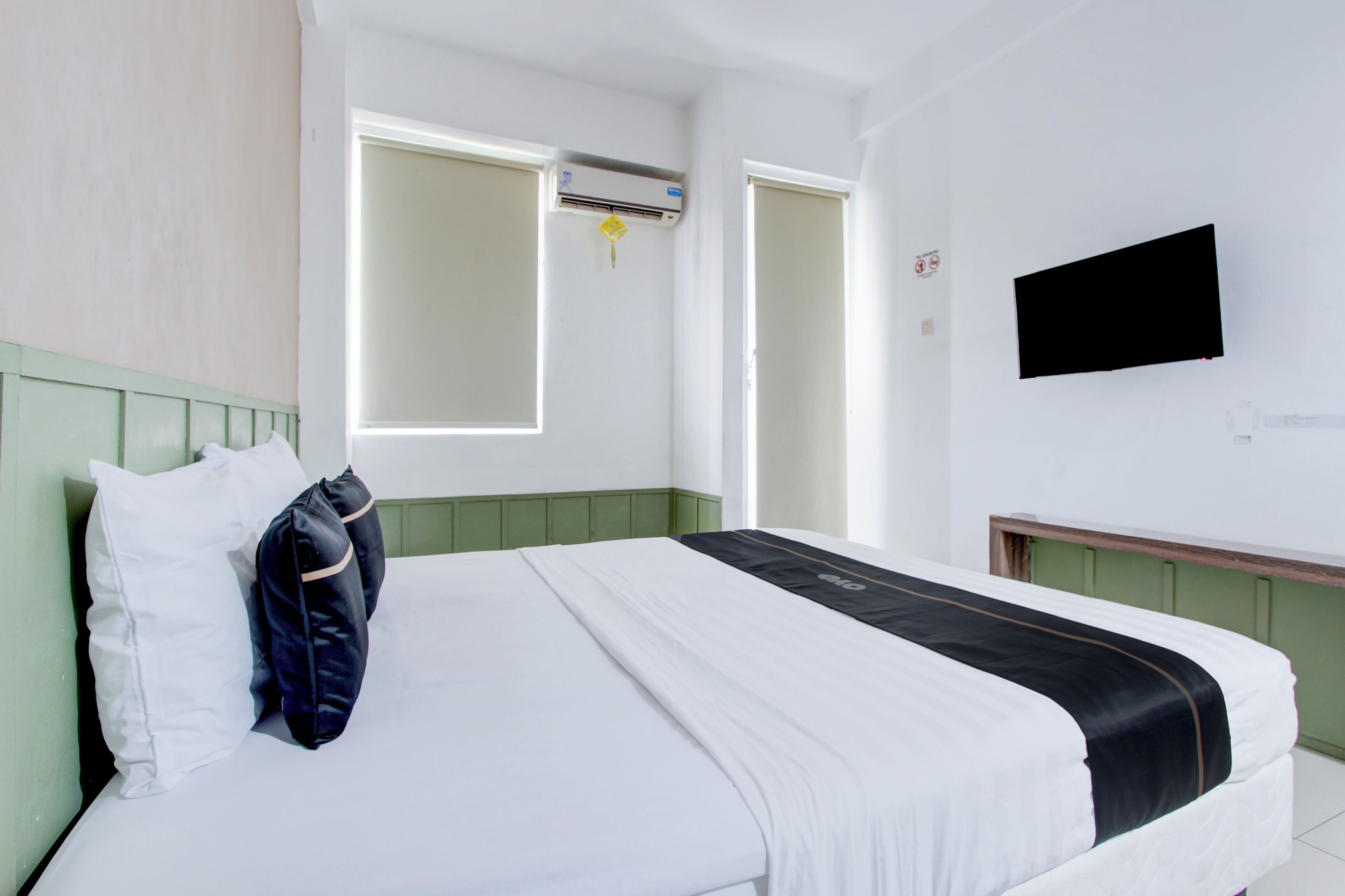 A hotel room with a bed, a TV mounted on the wall, and a window with blinds.