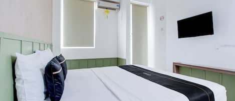 A hotel room with a bed, a TV mounted on the wall, and a window with blinds.