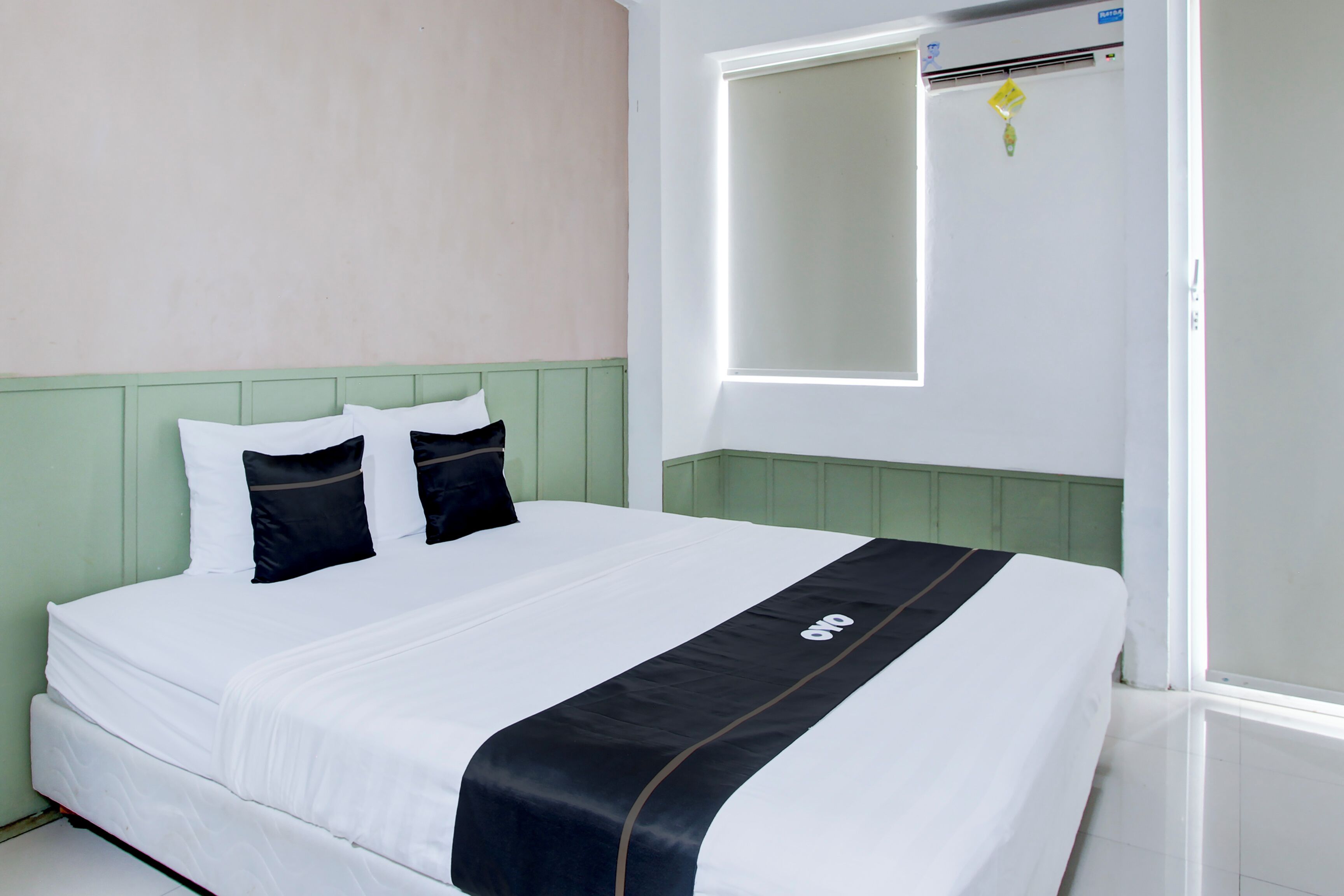 A neatly made bed with white bedding and a black accent, a green headboard, and a large mirror above it.