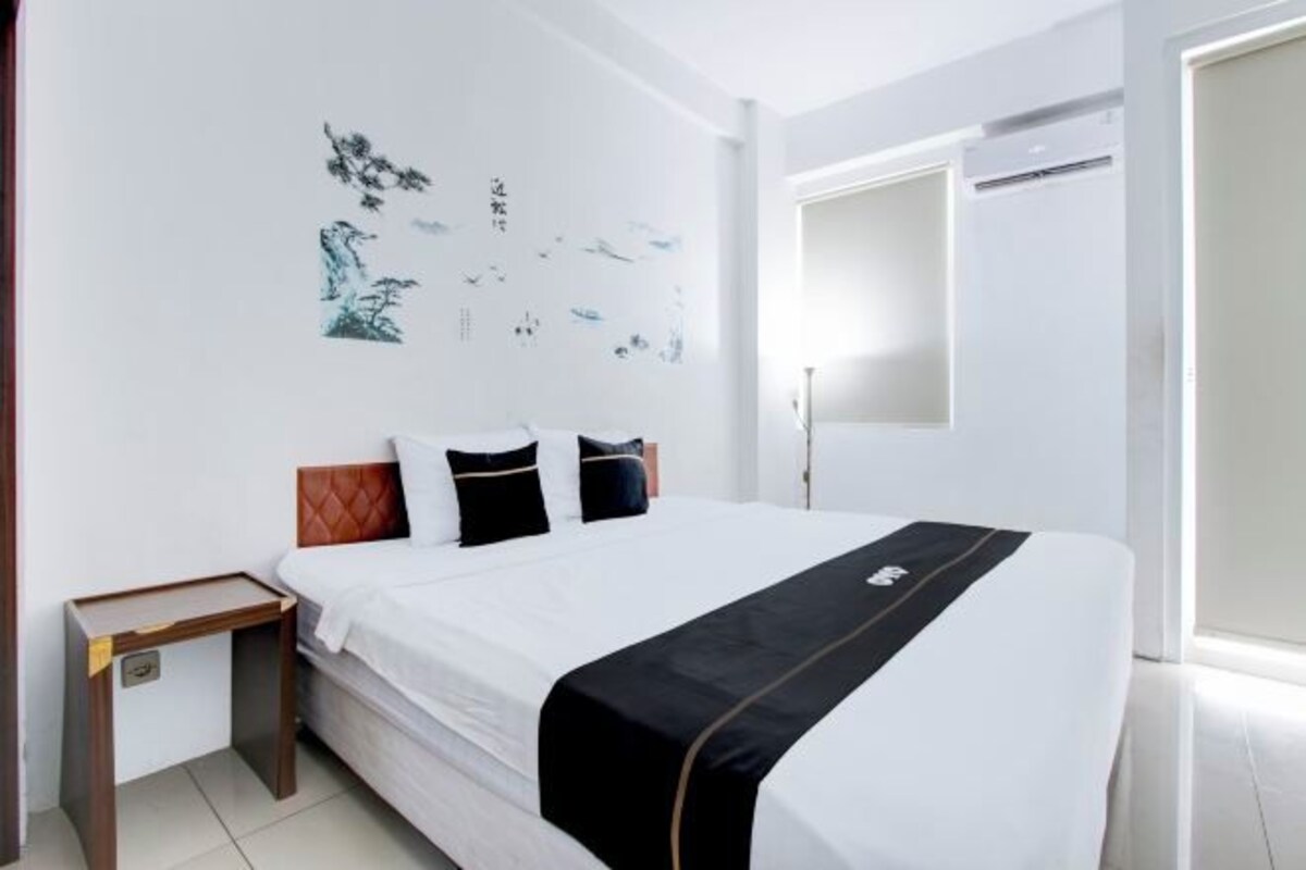 Ein Hotelzimmer mit einem Bett, einem Nachttisch, einer Wand mit Kunstwerken und einer Tür.
