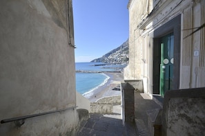 Un escalier étroit mène à une plage d’où l’on peut admirer la mer, et à un bâtiment dont la porte est peinte en vert.