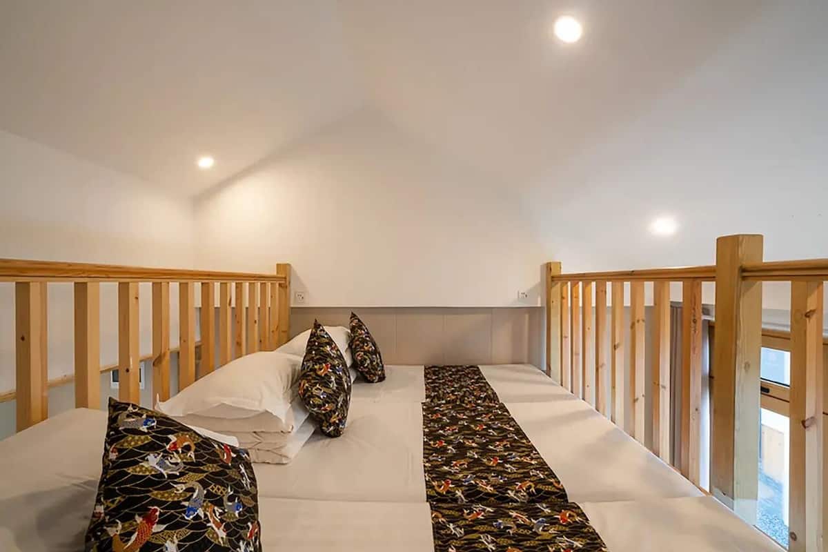 A bedroom with a wooden bunk bed, a patterned bedspread, and a view of the outdoors.