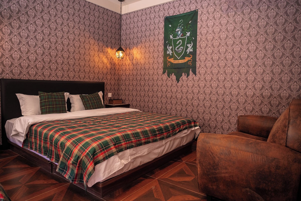 A bedroom with a bed, a chair, a patterned wallpaper, and a coat of arms on the wall.