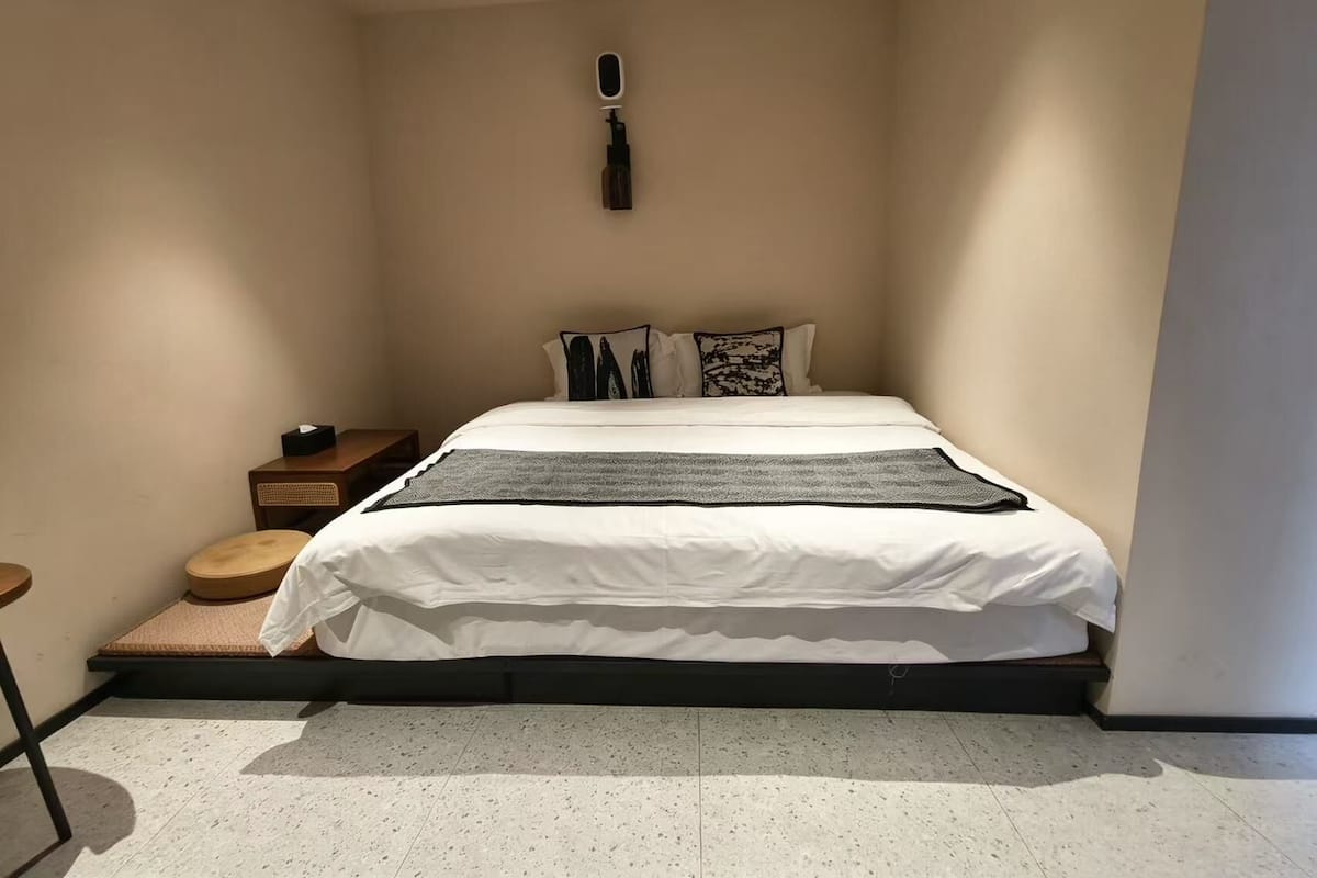 A bedroom with a bed, bedside tables, a wall-mounted light, and a small stool.