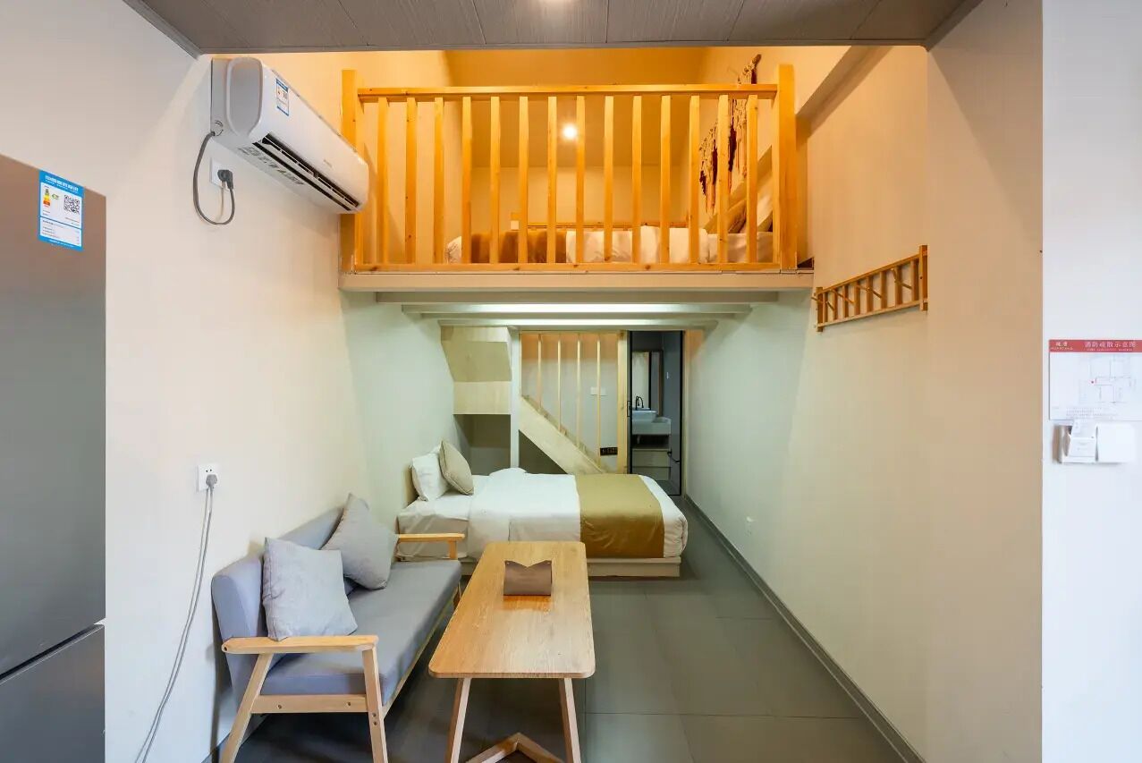 A compact room with a bunk bed, a sofa, a small table, and a staircase leading to an upper level.