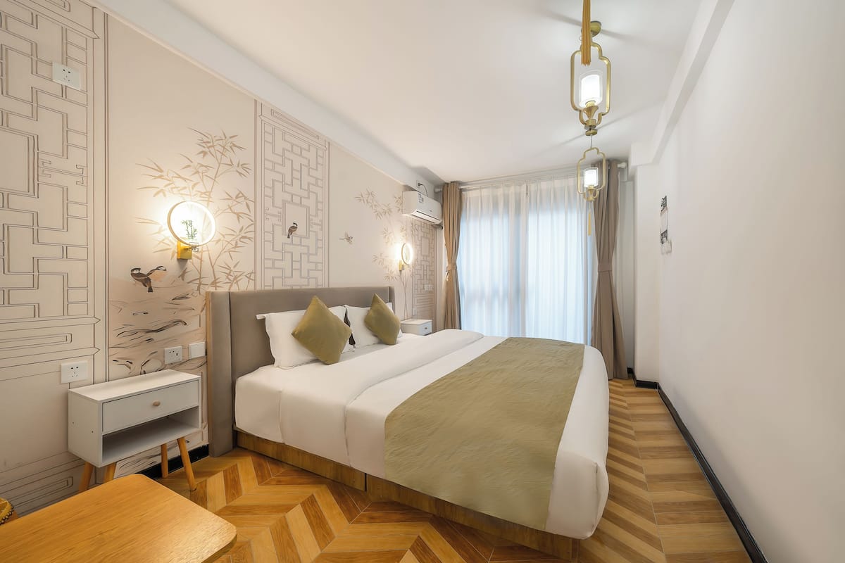 A modern hotel room with a large bed, bedside lamps, a nightstand, and a herringbone-patterned floor.