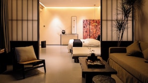 Une chambre d’hôtel moderne, équipée d’un canapé, d’un fauteuil, d’un lit, d’une table de chevet et d’une grande plante en pot.