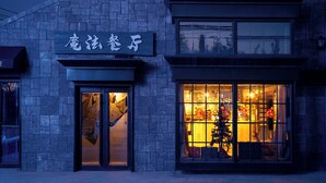 Un bâtiment doté d’une façade en pierre, d’une enseigne avec des caractères chinois et d’une fenêtre laissant entrevoir l’éclairage et les décorations intérieures.