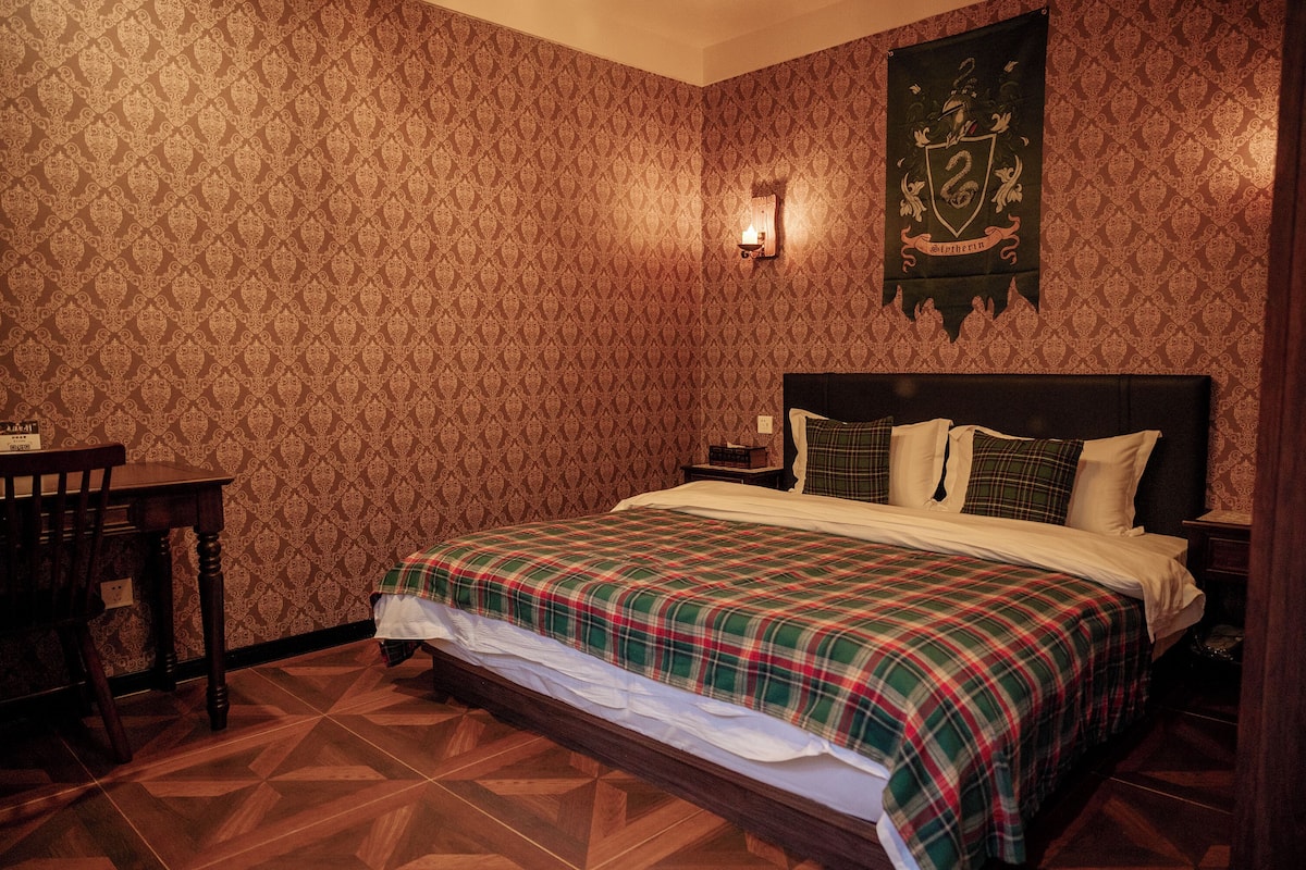 A room with a patterned wallpaper, a bed with a plaid bedspread, a nightstand with a lamp, and a wooden chair.