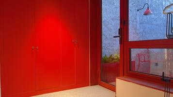Una habitación con un armario rojo, una ventana con vistas a plantas y una lámpara roja.