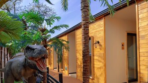 Une statue de dinosaure, un bâtiment en bois avec des portes et un palmier.