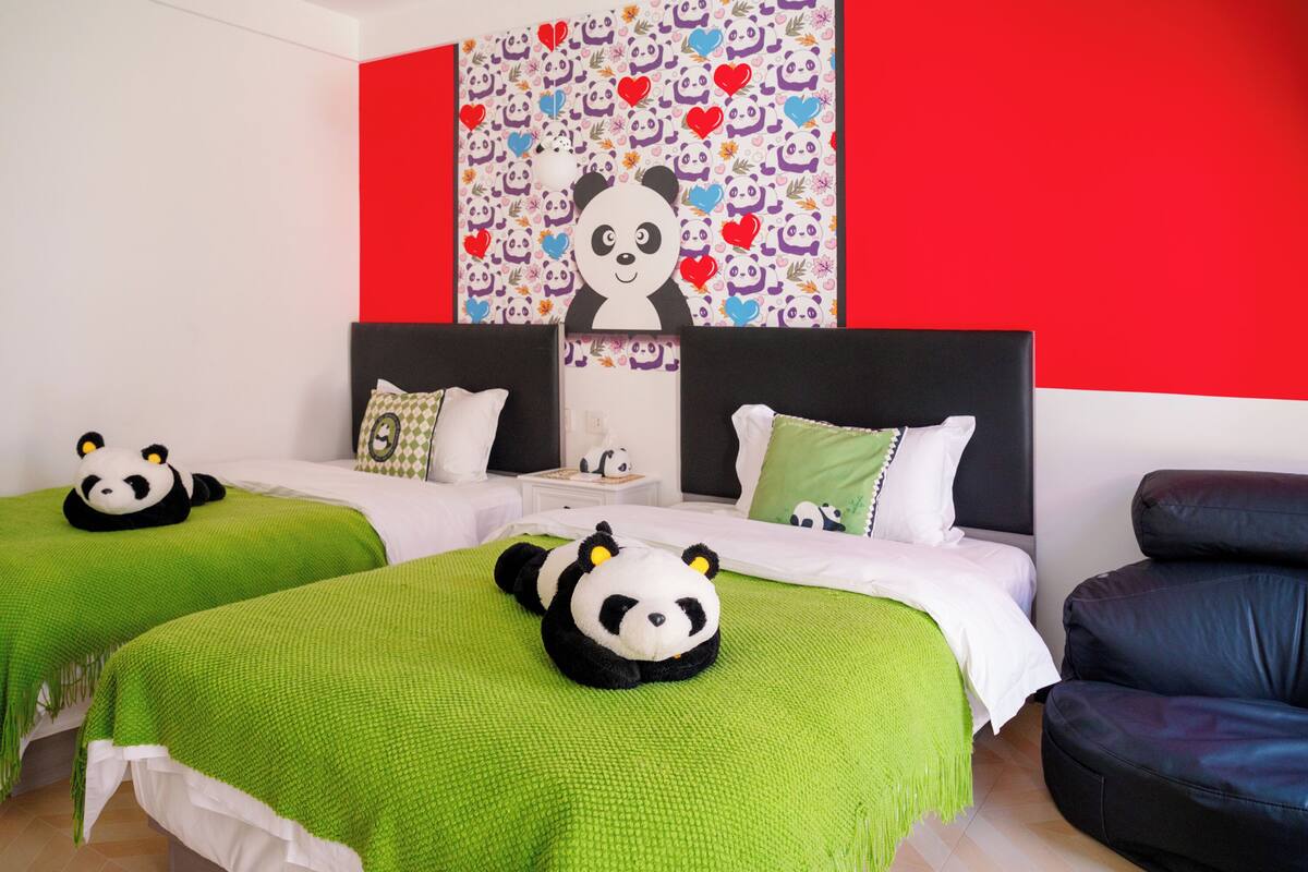 A hotel room with two beds, green bedding, a panda-themed headboard, and a red and white wall.