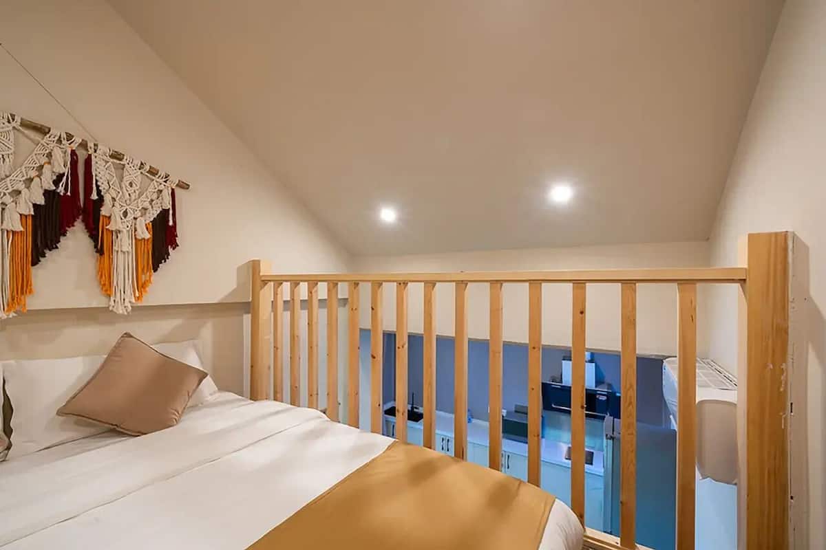 A bedroom with a bed, a wooden headboard, and a view of a kitchen area.