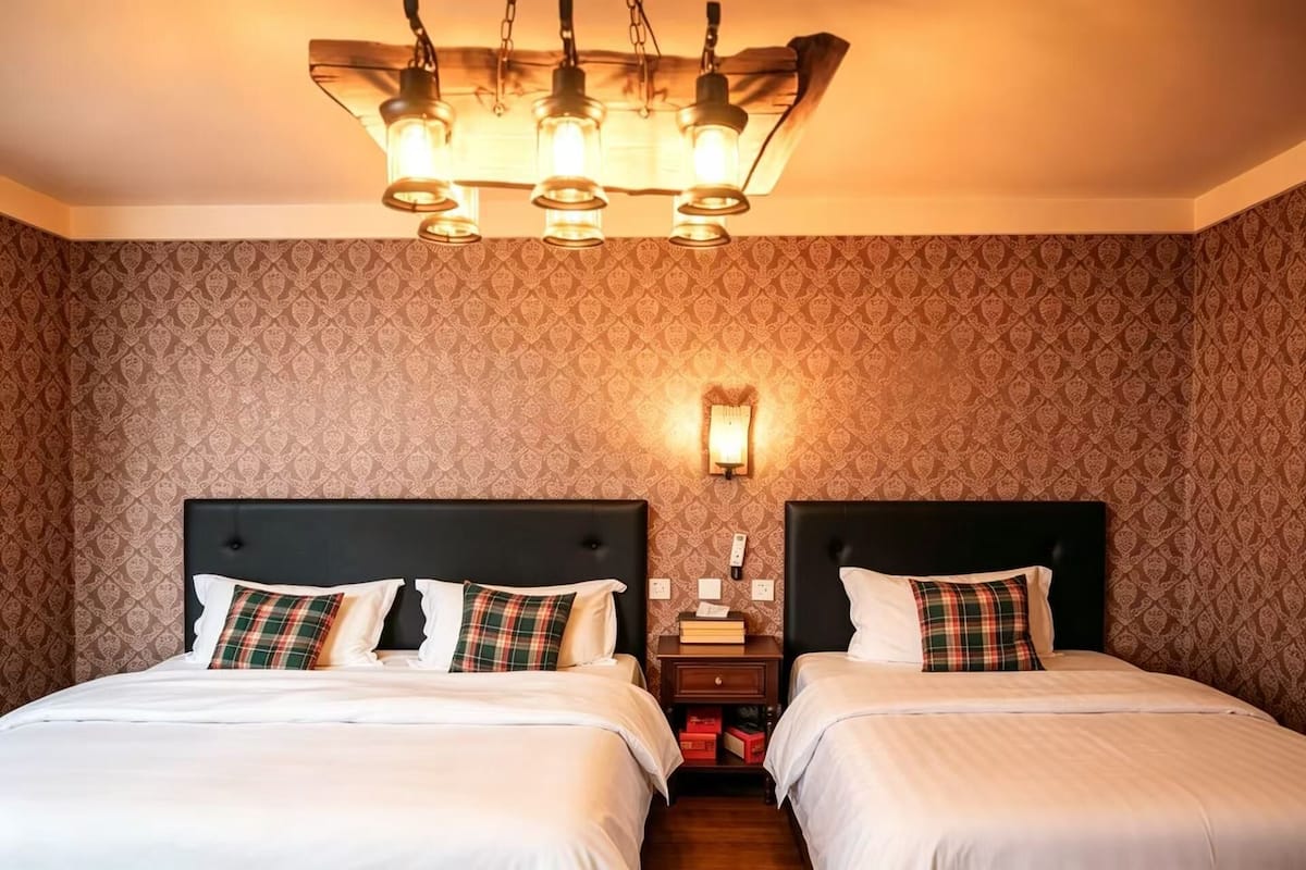 A hotel room with two beds, a chandelier, a nightstand, and patterned wallpaper.