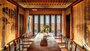 Une salle à manger de style japonais traditionnel, avec une longue table en bois, des chaises et une vue dégagée grâce à de grandes fenêtres.