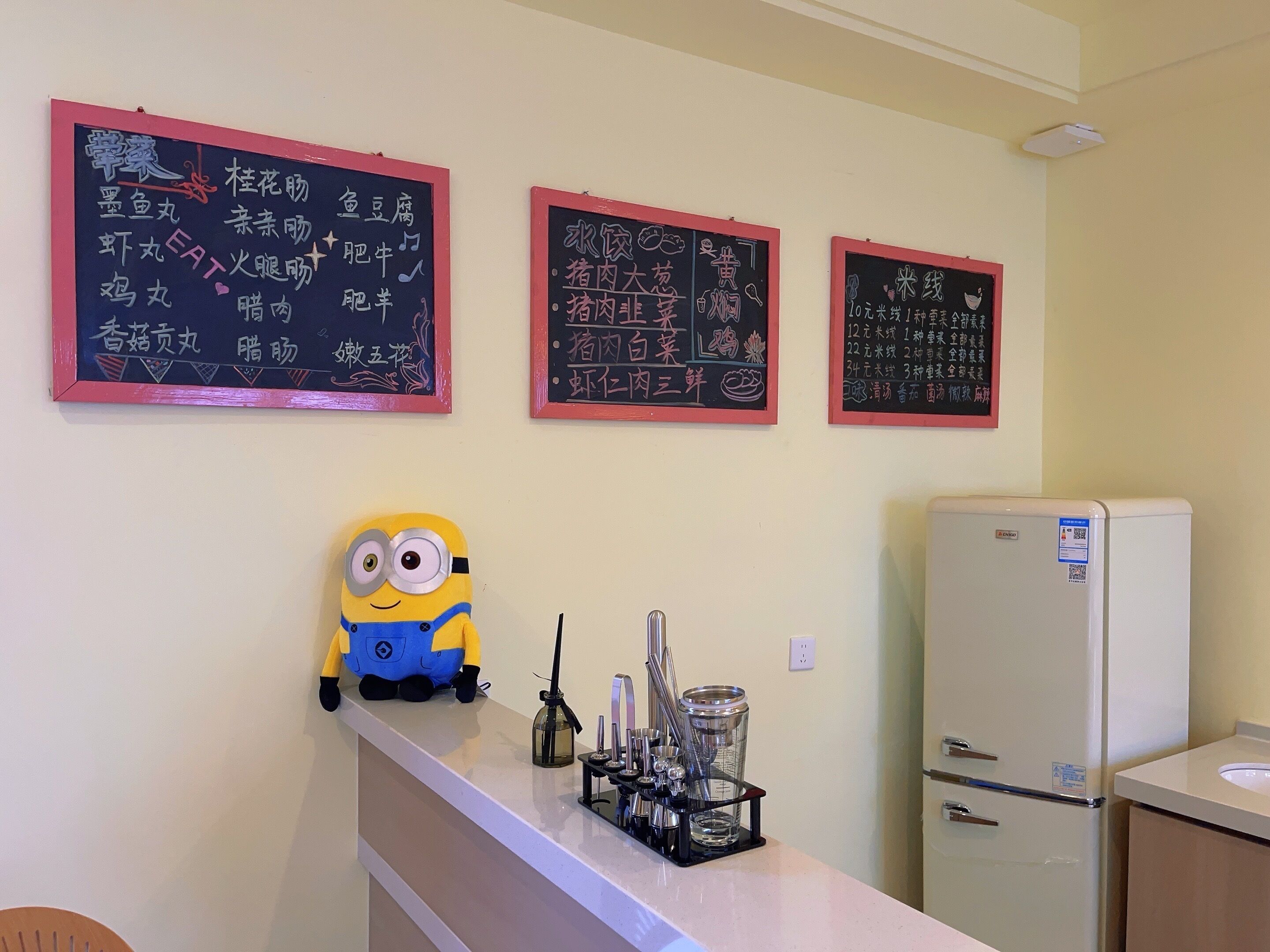 A kitchen with a white refrigerator, a counter with a coffee maker, and three chalkboard menus on the wall.