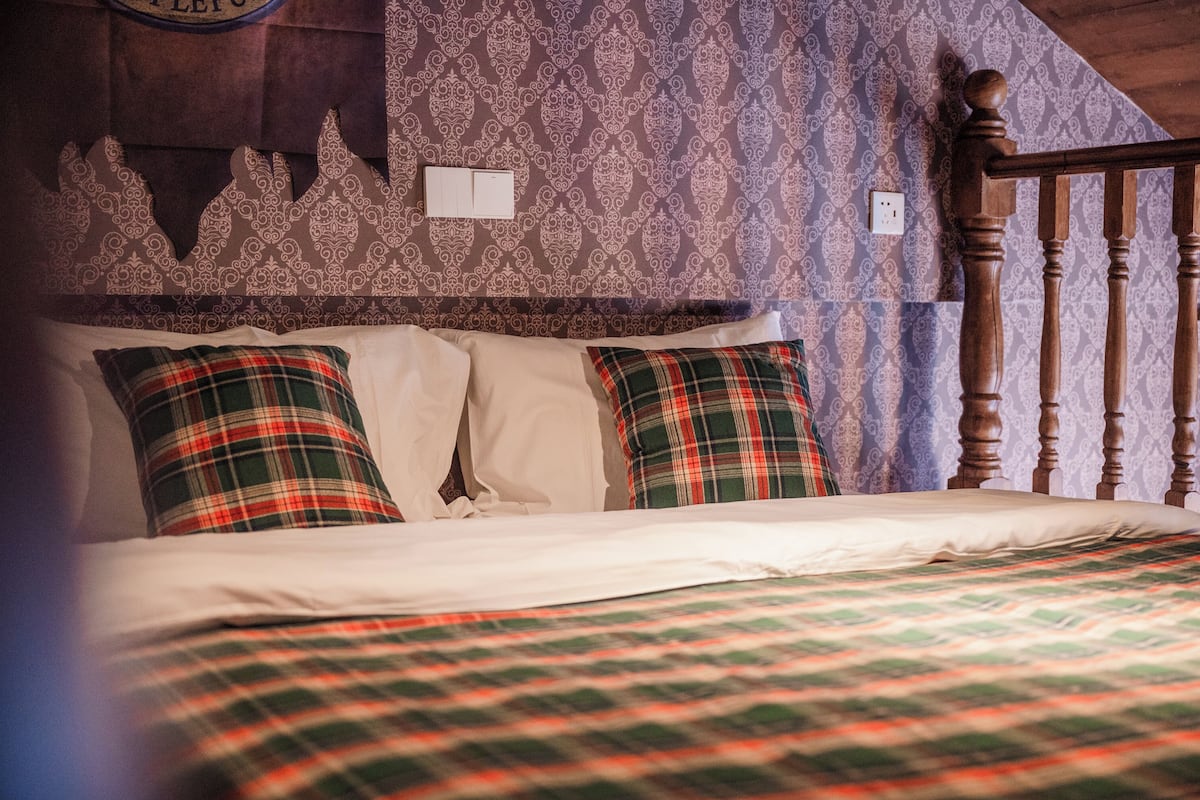 A bed with plaid bedding, a wooden headboard, and patterned wallpaper.
