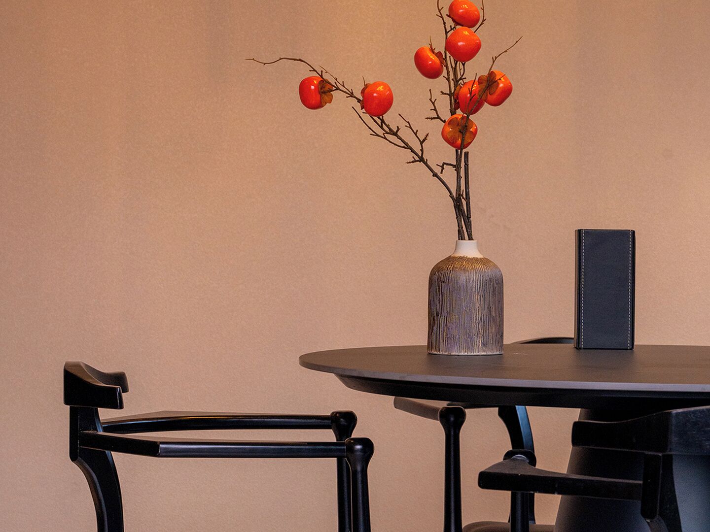 A round table with a vase of red berries and a black object beside it.