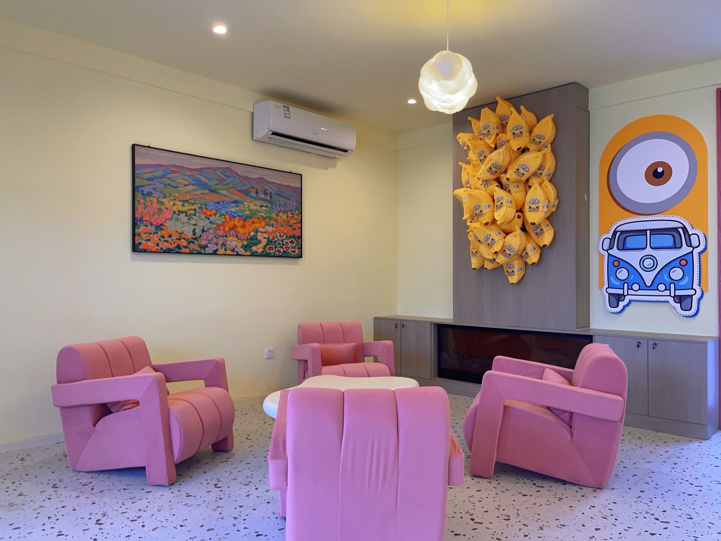 A room with pink chairs, a painting, an air conditioner, and a wall decoration.