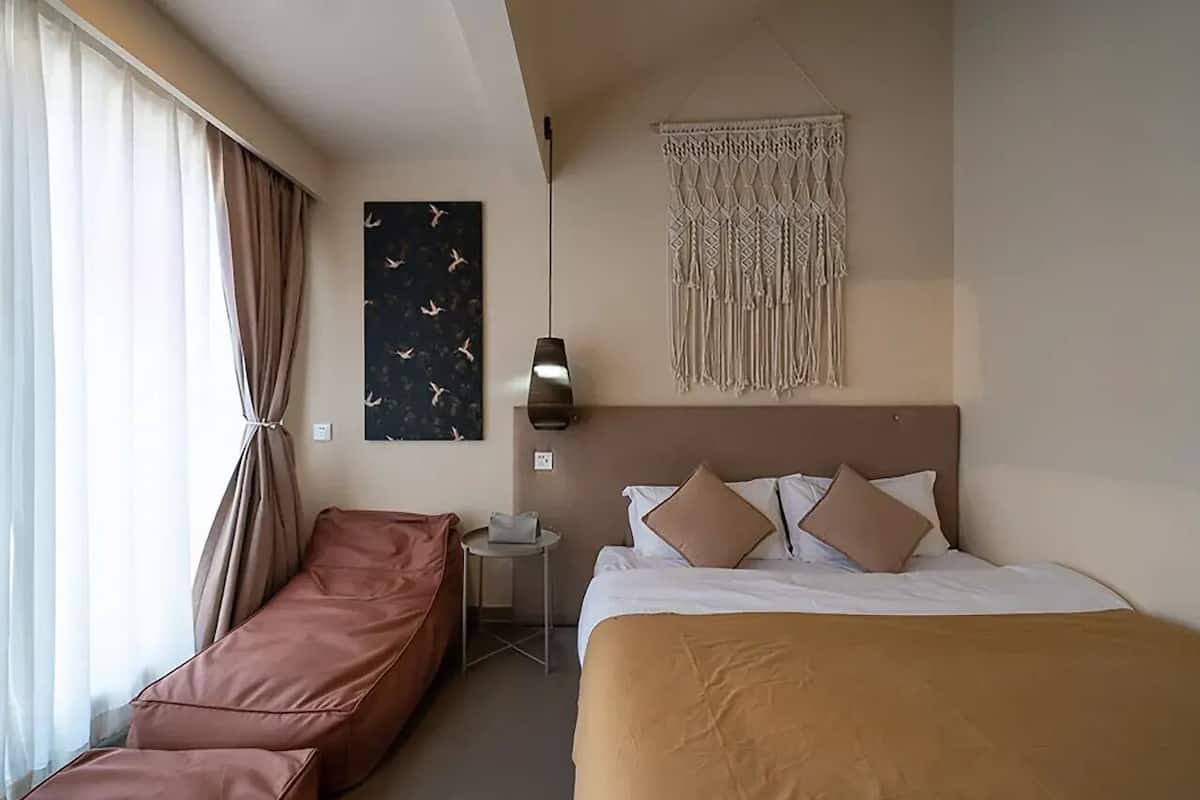 A hotel room with a bed, a sofa, a wall-mounted macrame piece, and a painting.