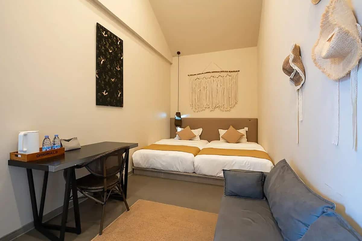 A hotel room with a bed, a desk, a chair, a sofa, a wall-mounted hat rack, and a decorative macrame piece.
