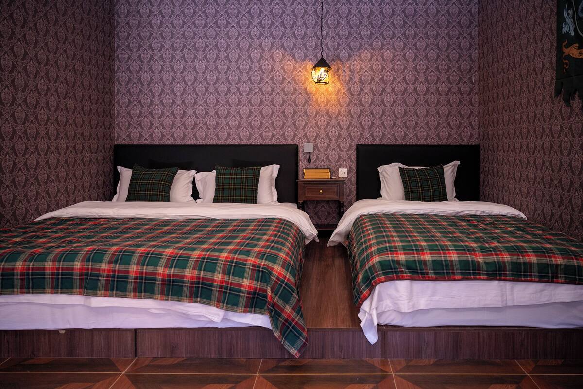 A room with two beds, each with a plaid bedspread, a nightstand with a lamp, and patterned wallpaper.