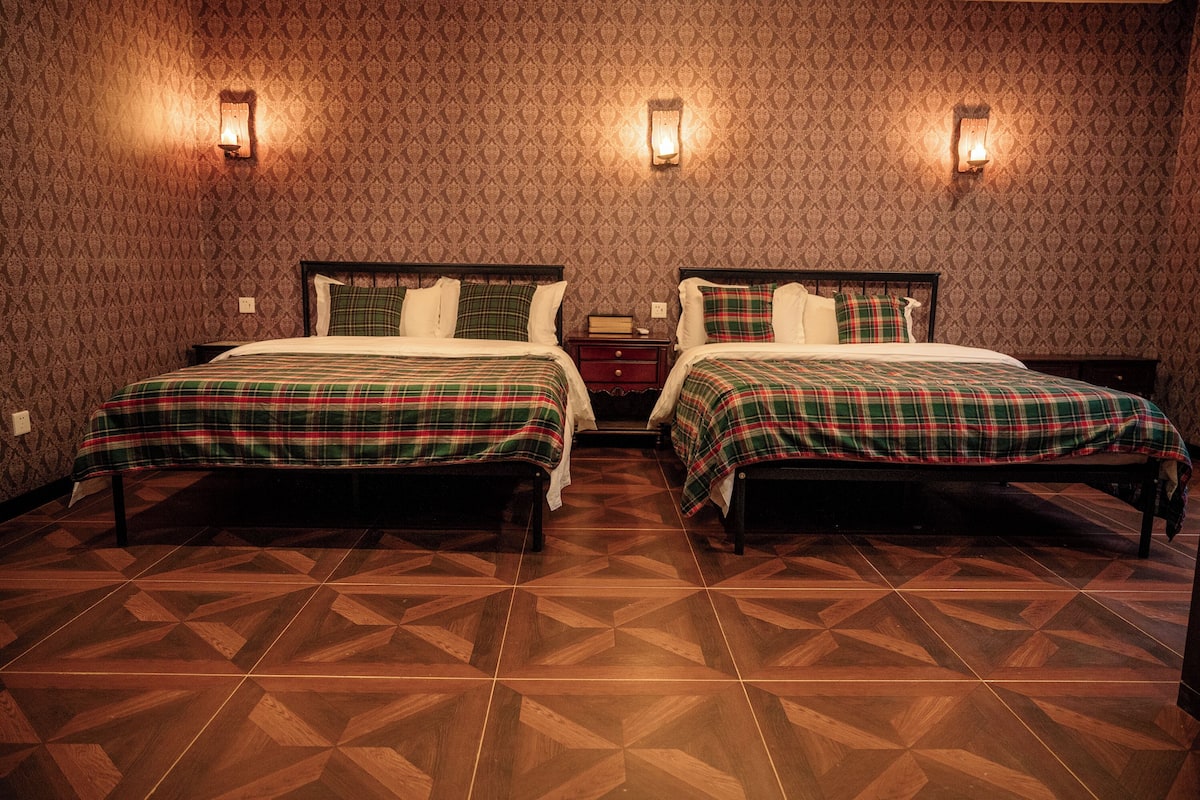 A room with two beds, patterned wallpaper, and a geometric tile floor.