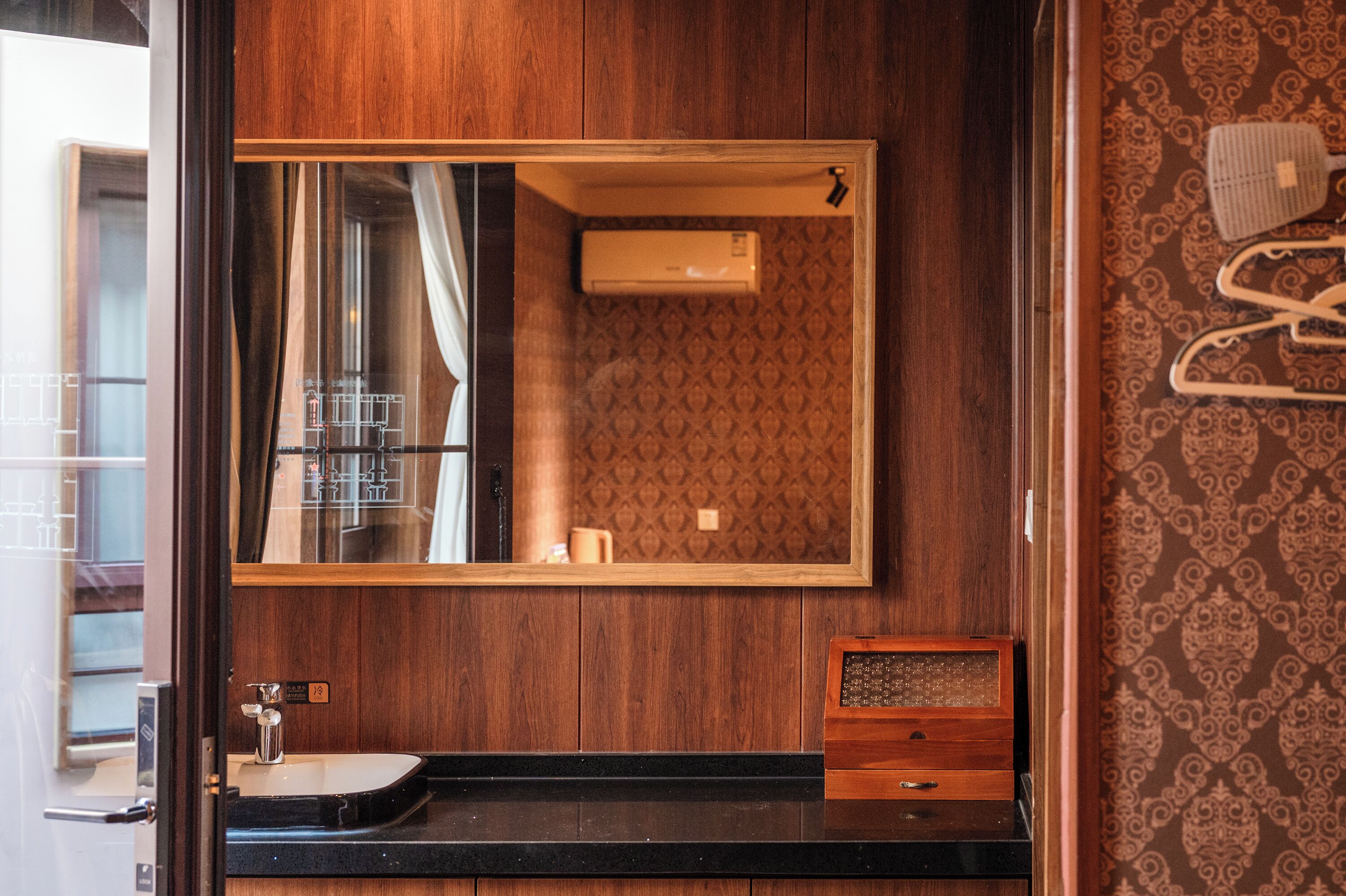 Un baño con tocador de madera, un espejo, un perchero para toallas y un papel tapiz estampado.