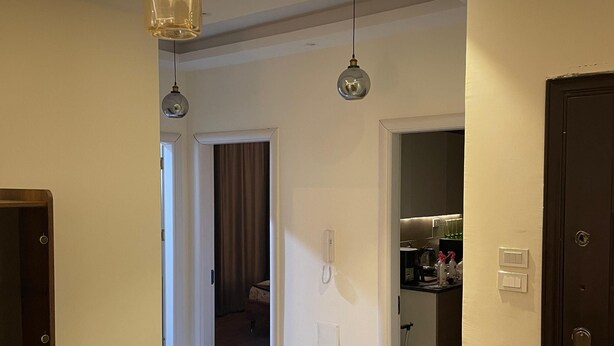 Ein moderner Essbereich mit einem Holztisch und Stühlen, im Hintergrund eine Küche und Pendelleuchten.