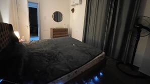 Ein Hotelzimmer mit Bett, Nachttisch, Kommode und Standventilator.