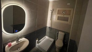Ein Badezimmer mit rundem Spiegel, Waschbecken mit rosa Seifenspender, Badewanne und Toilette.