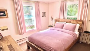 A bedroom with a wooden bed, pink bedding, a wooden nightstand, a small table with a bottle, and a striped rug.