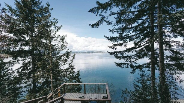 A wooden deck overlooking a calm lake, surrounded by tall evergreen trees.