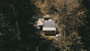An aerial view of a cabin surrounded by dense forest, with a clear sky above.