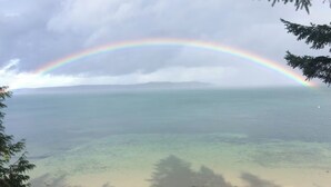 A mug on a wooden table with a view of a beach and a rainbow over the ocean.