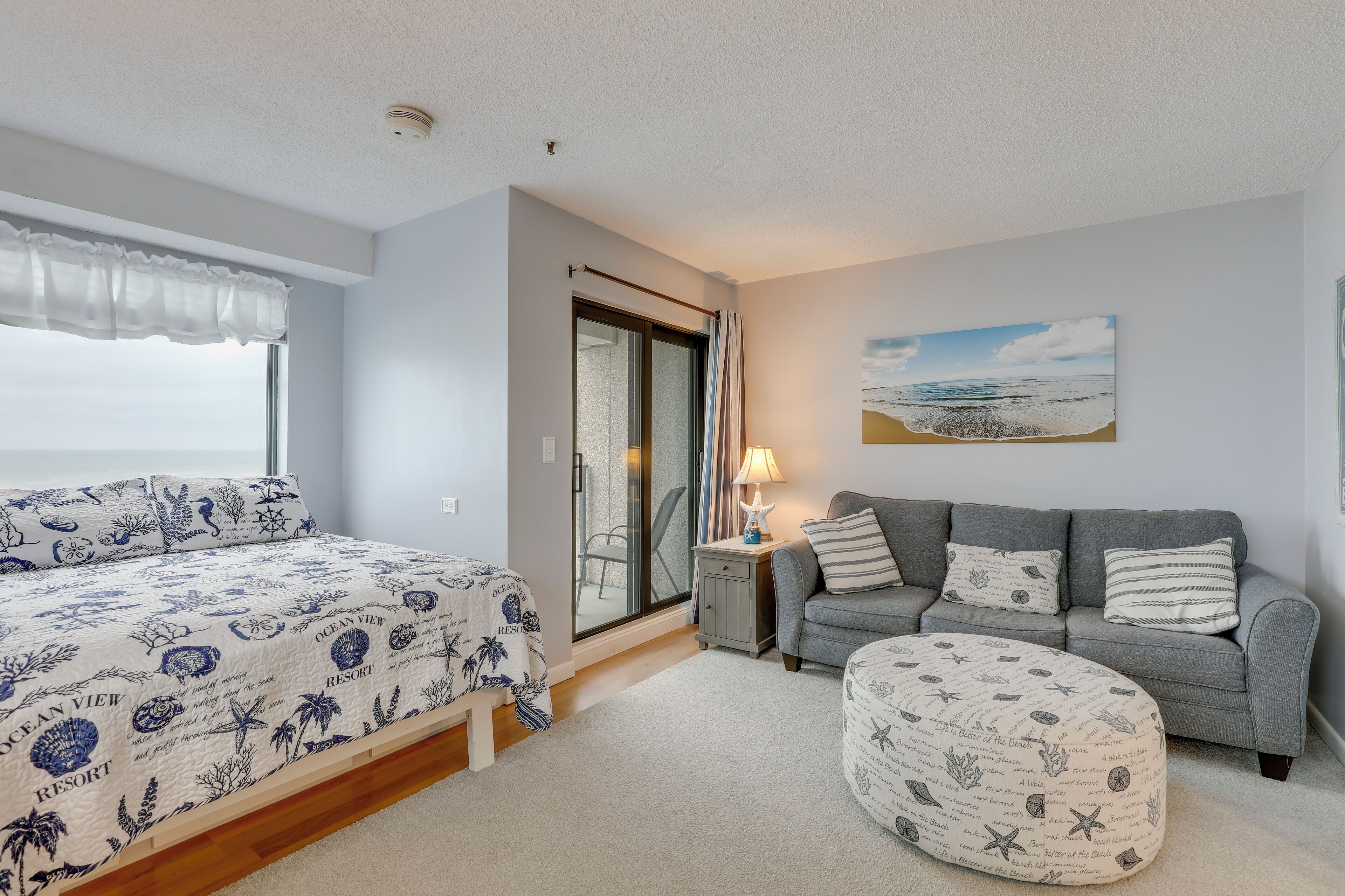 Een slaapkamer met een bed, een grijze bank, een bijzettafeltje en een raam met uitzicht.
