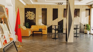 A modern lobby with a sofa, chairs, a flag, and a framed picture. - Palmiers Hôtel Club (Errachidia)
