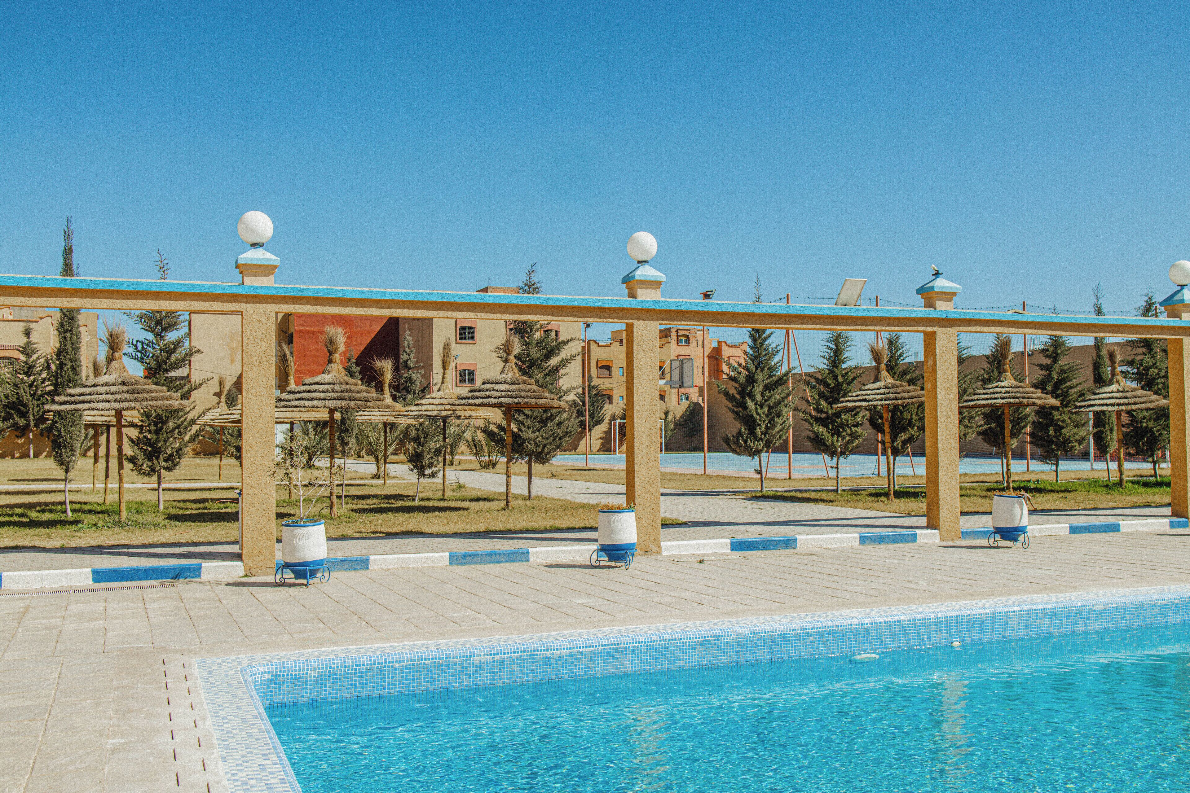 A swimming pool with a tiled edge, surrounded by a pergola with spherical decorations, and palm trees in the background.