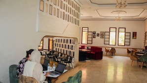 A spacious indoor area with multiple seating arrangements, including tables and chairs, and a staircase leading to an upper level. - Palmiers Hôtel Club (Errachidia)