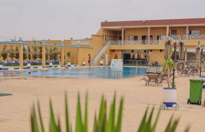 Zona de piscina con sillas de descanso y sombrillas, una escalera que lleva a un edificio y un contenedor de basura.