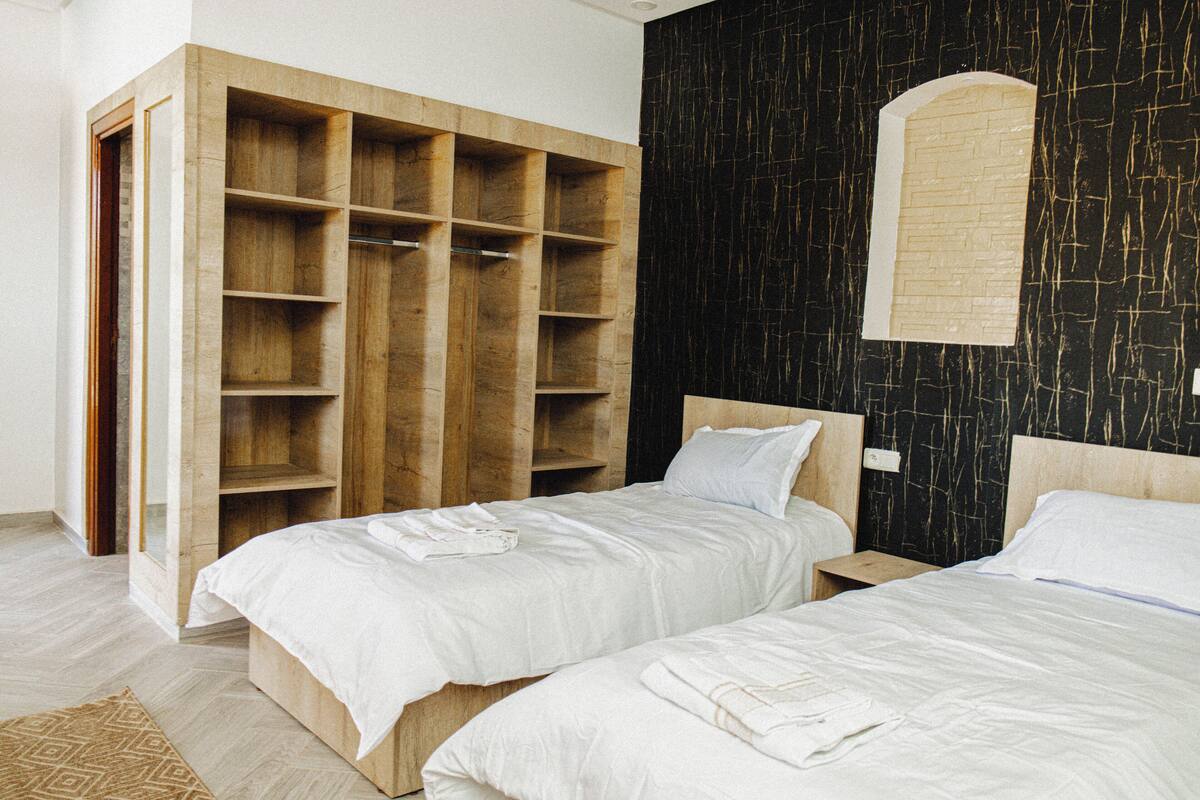A bedroom with two beds, a wooden wardrobe, and a black wall with a window.