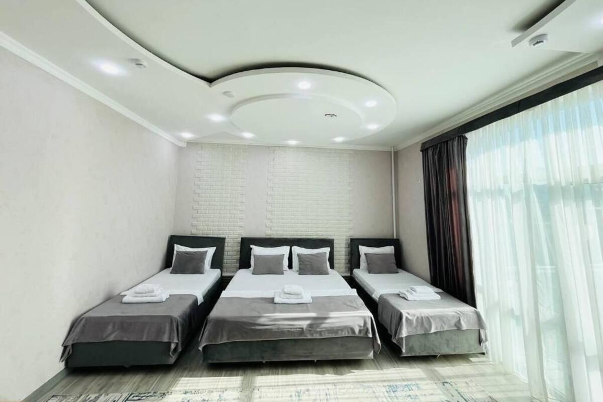 Une chambre d’hôtel avec trois lits, un mur en briques blanches et une grande fenêtre avec des rideaux.